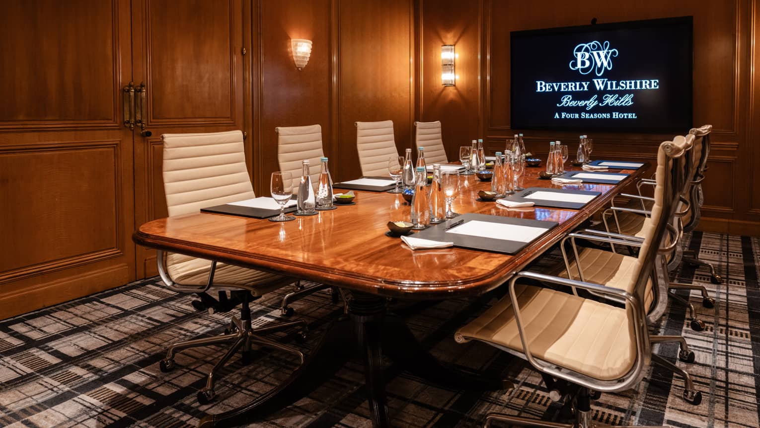A meeting room with a table set with glasses and papers, and a monitor on the wall
