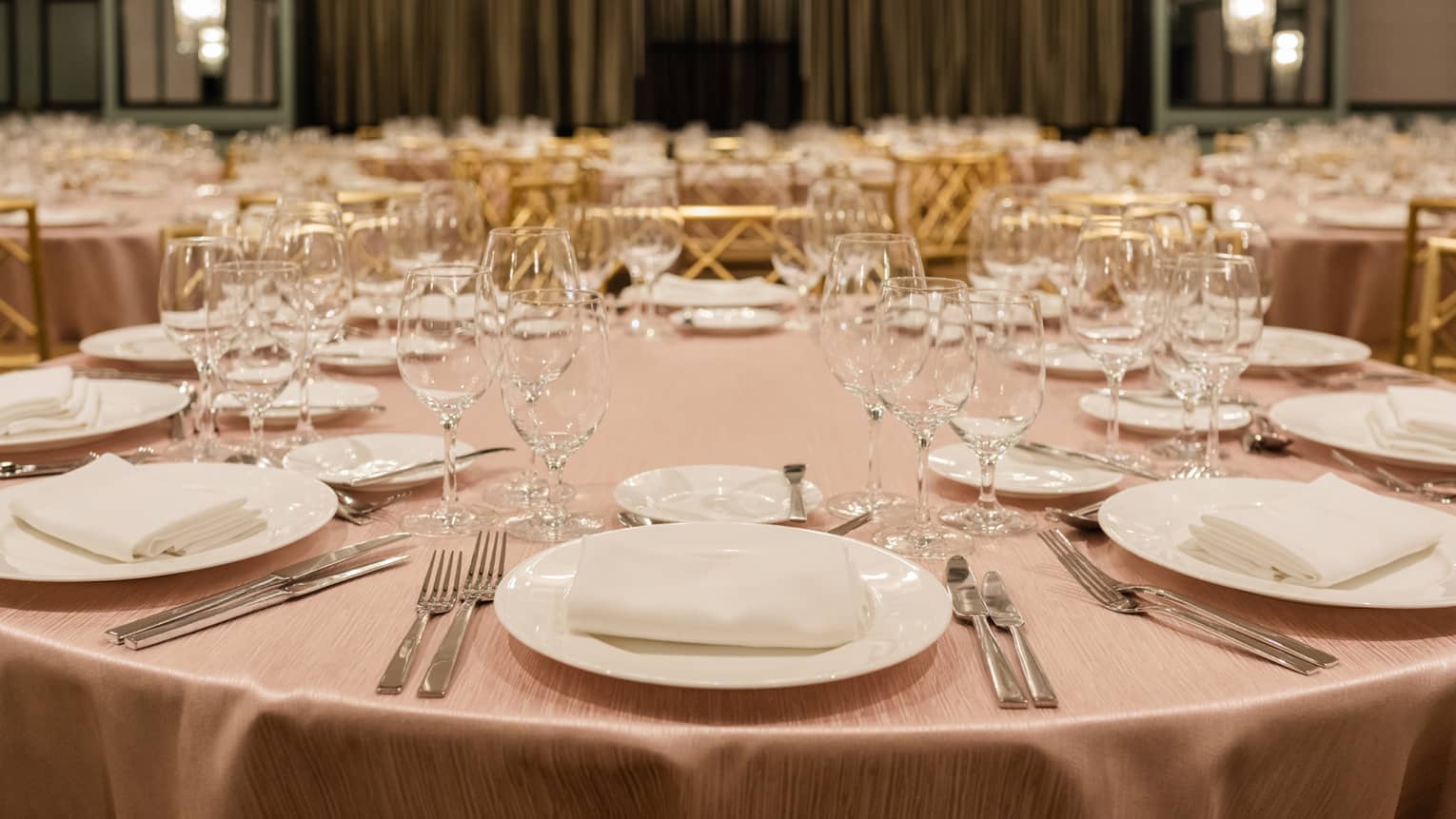 A table with a pink tablecloth set with silverware, glasses and plates