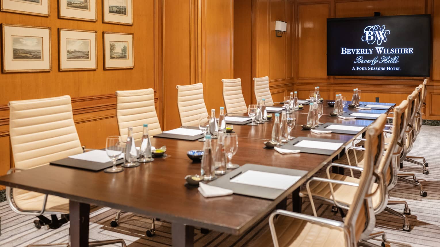A meeting room with pictures hanging on the wall and a rectangular table with pens and papers at each seat