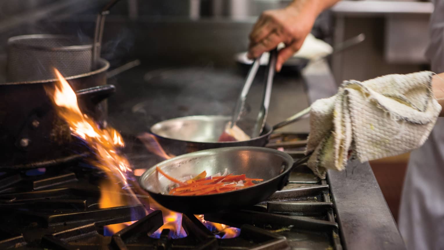 Chef sautéing vegetables in a professional kitchen over open flame