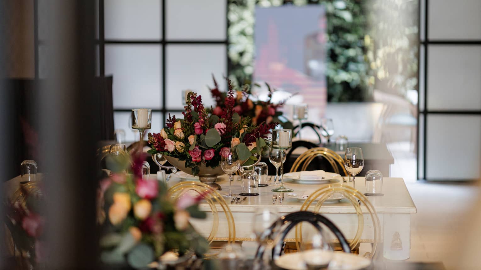 Large white wood table in teh centre of a meeting room topped with burgundy, peach and green floral with a screen door that opens up to a terrace in the background