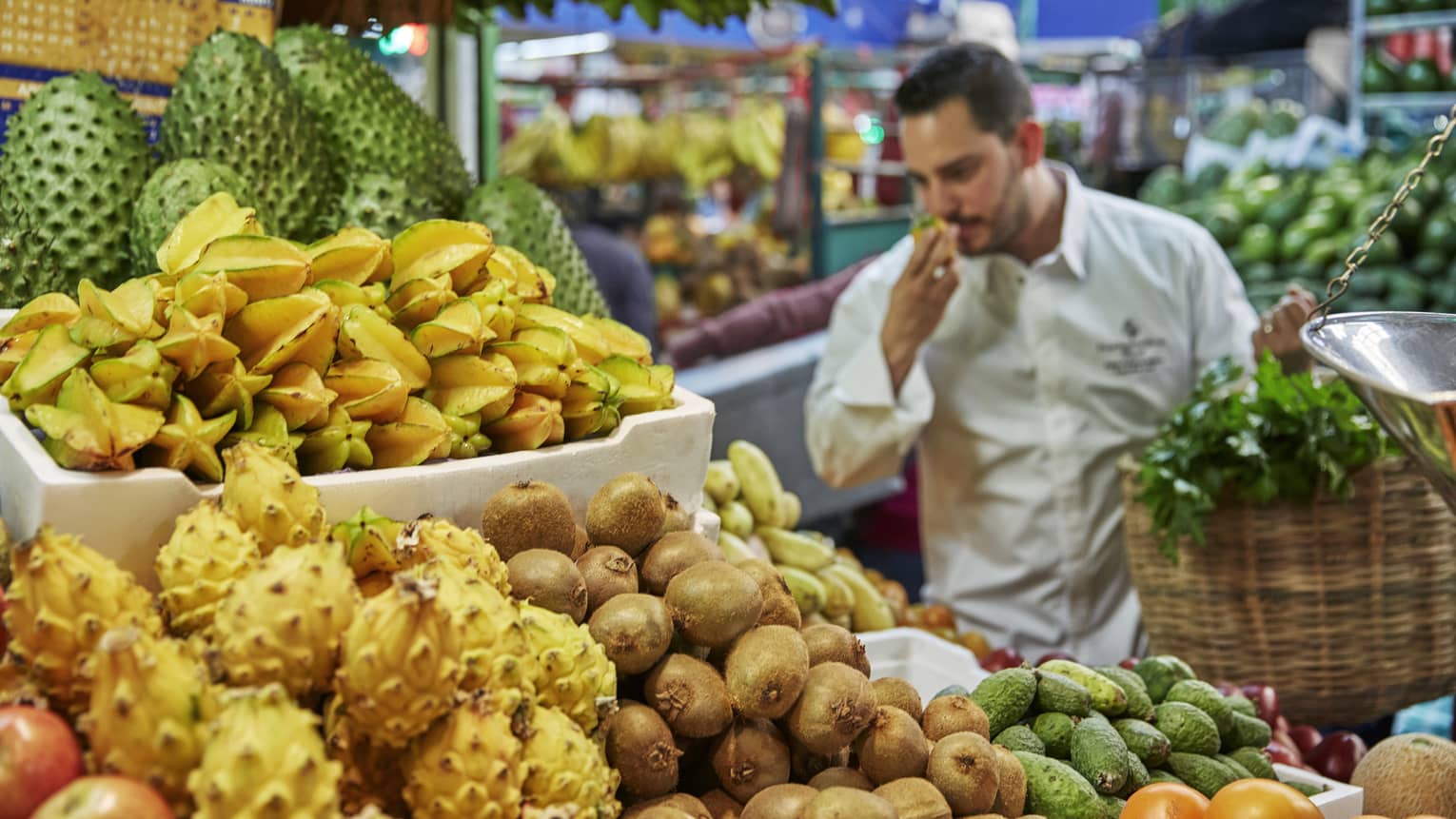 Chef smells tropical fruit at stand in market 