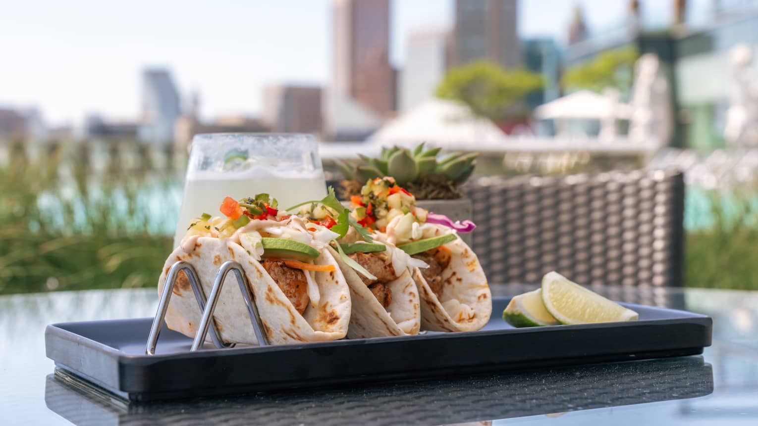 Three tacos with sliced lime on the side.