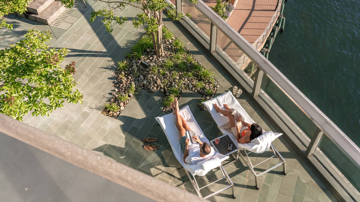 Two guests laying in lounge chairs outside near a river