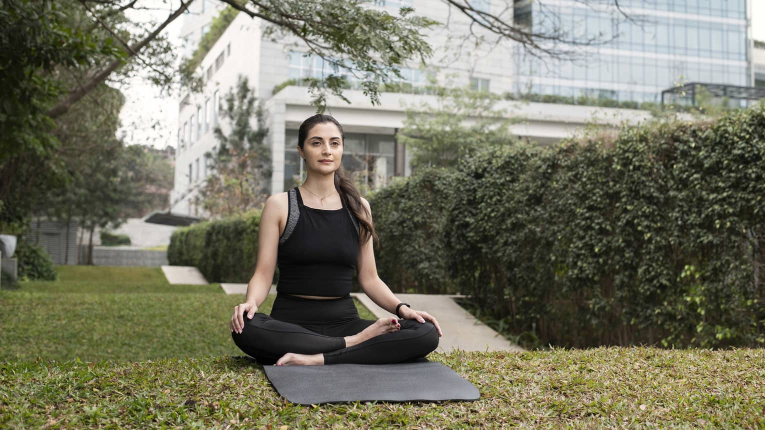 Person wearing athletic clothes and sitting on a yoga mat with their legs crossed.