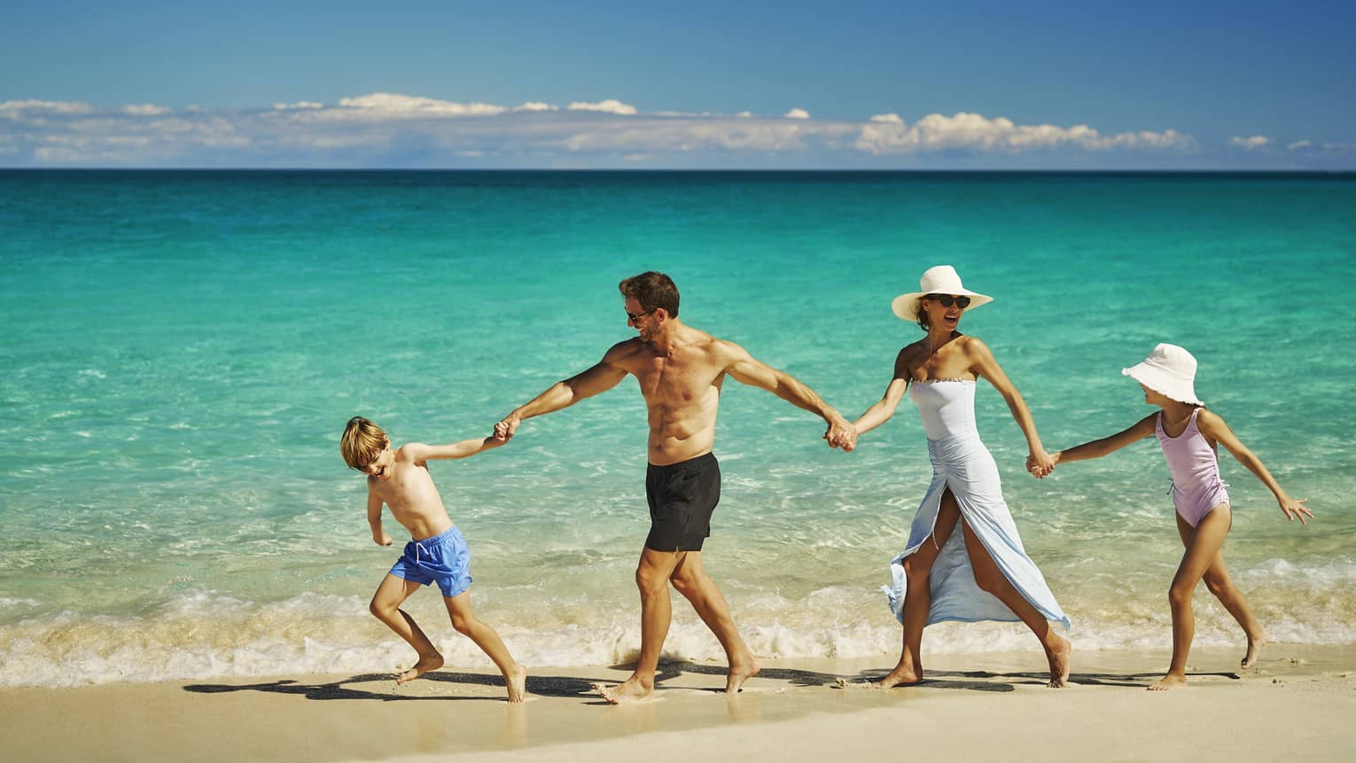 Family holding hands while walking on the shore of the blue ocean.