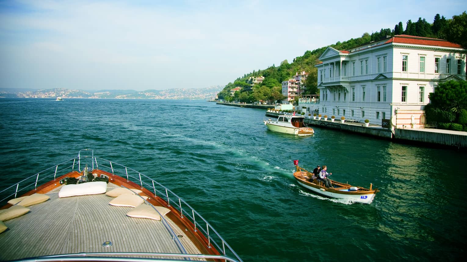 Front of boat on water, passing smaller boat and white building exterior