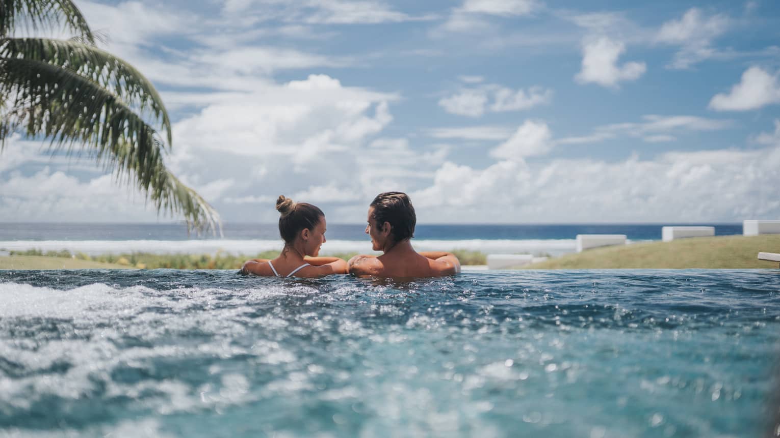 Back of couple at edge of whirlpool overlooking ocean, blue sky 