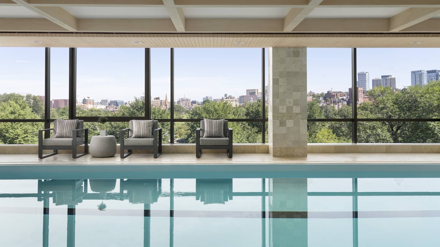An indoor pool surrounded by large windows with lounge chairs nearby.
