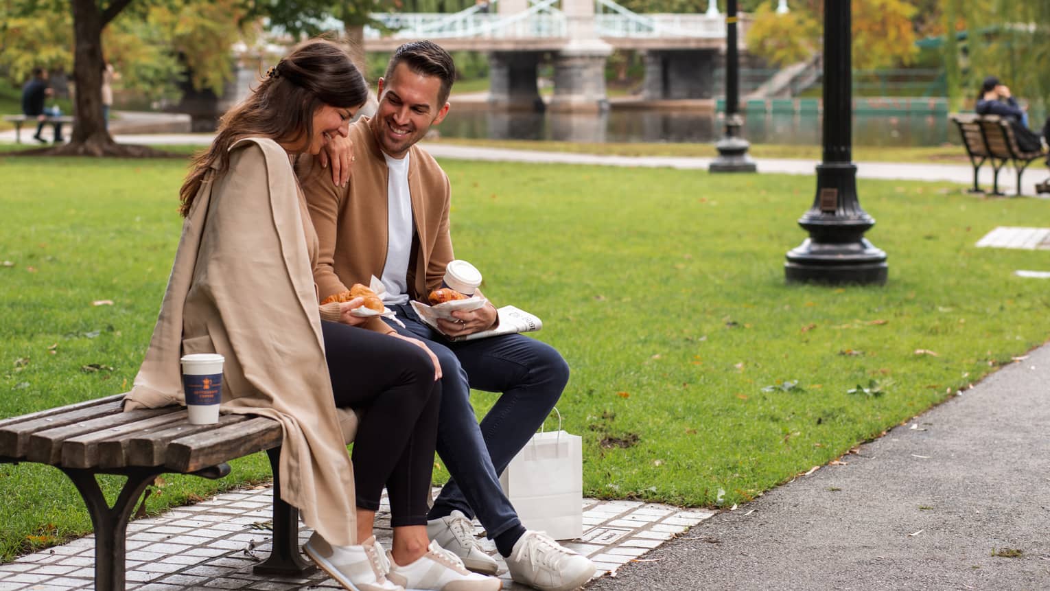 A man and woman sitting on a park bench with a river nearby.