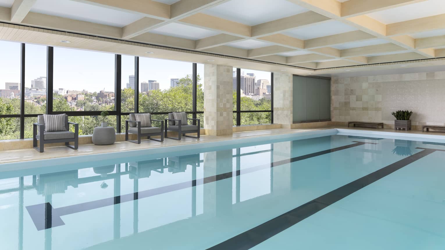 A large indoor pool with large windows and a small sitting areas.