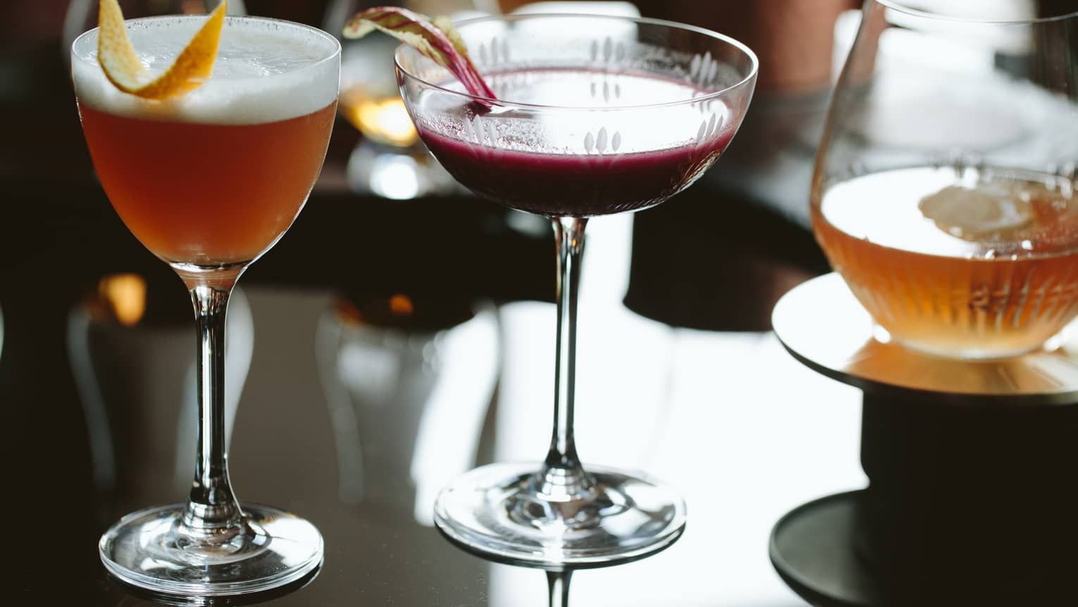 Three gourmet fall cocktails in glasses with rind garnishes 