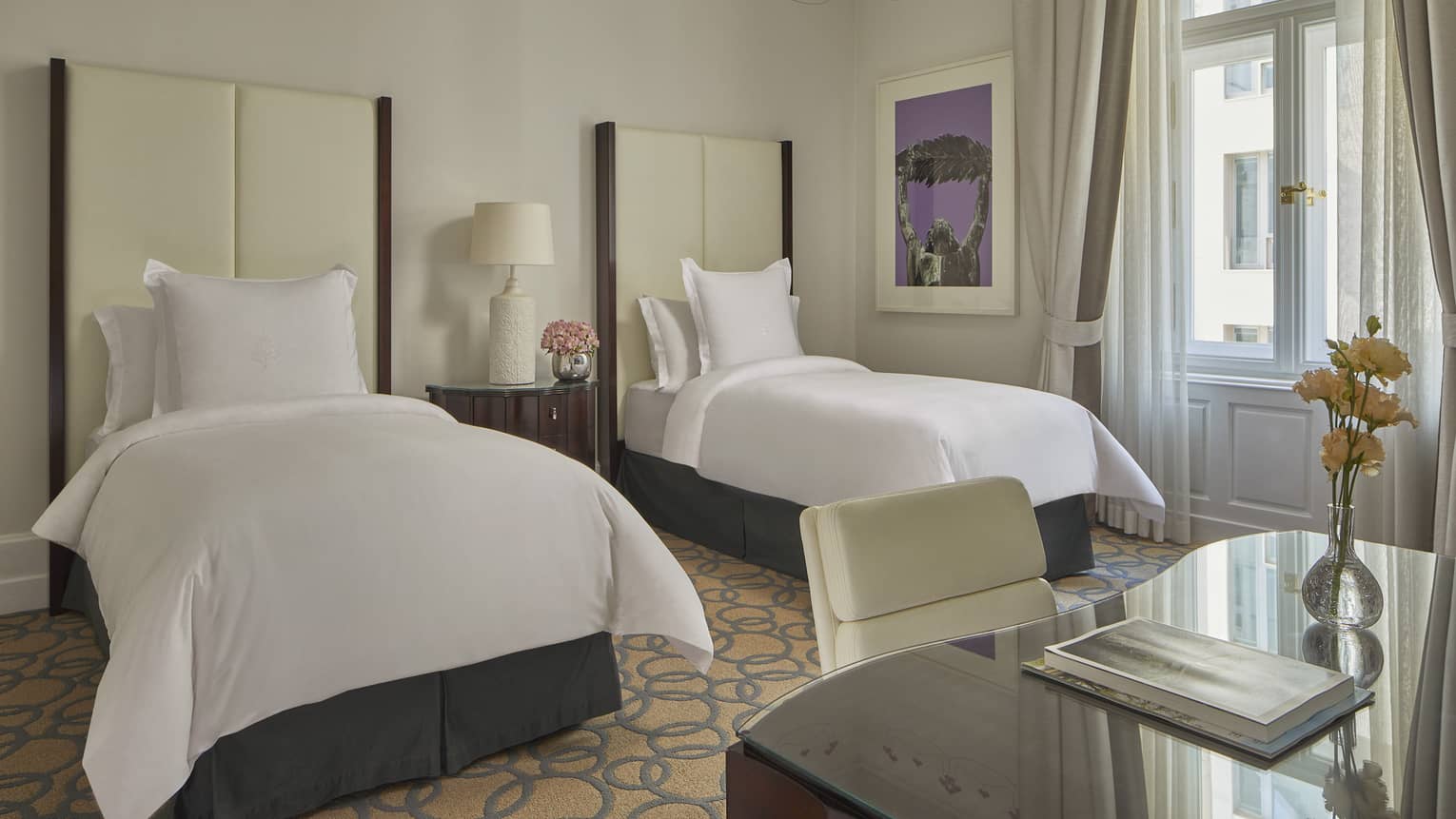 Room with two white twin beds with tall headboards and desk with chair