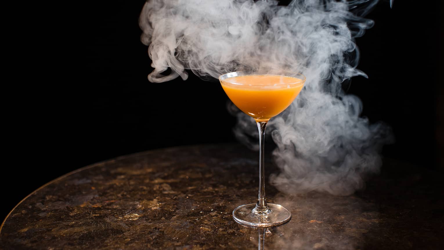 Orange cocktail in martini glass surrounded by smoke
