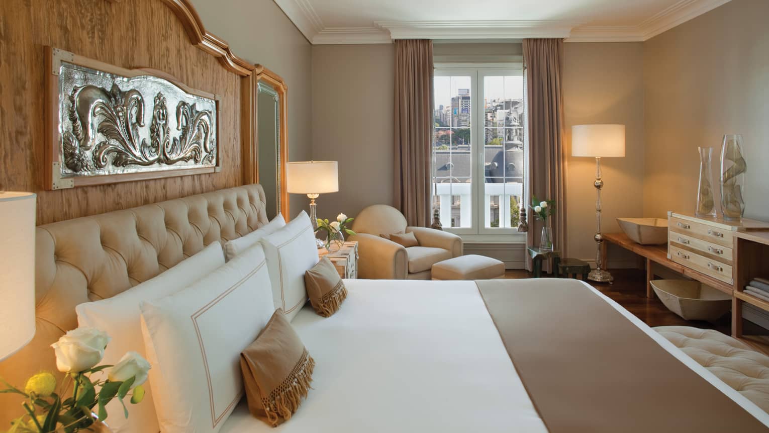 Owner Suite bed with tall wood headboard and silver plaque, white armchair by window