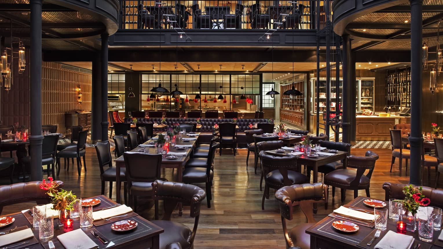 Two-storey restaurant dining room with dark leather chairs and tables under curved black balconies 