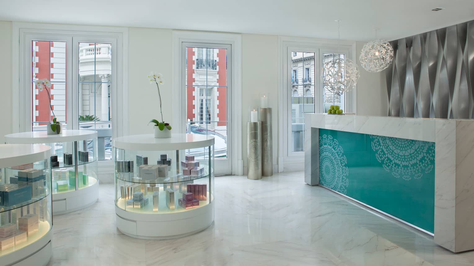 White marble spa lobby with round glass display cabinets, desk with teal pattern, white lamp