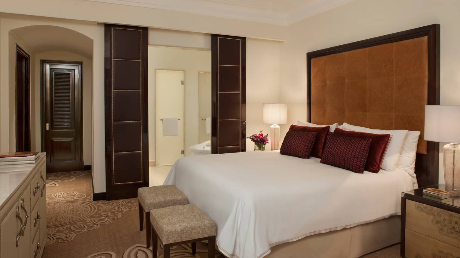 E-Lounge One Bedroom Suite bed with tall padded brown headboard, leather wall panels, two small benches