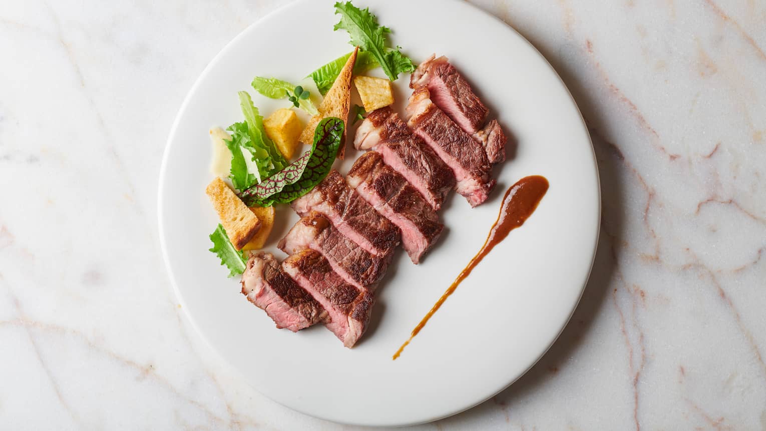 Strips of seared beef on plate with salad, sauce garnish