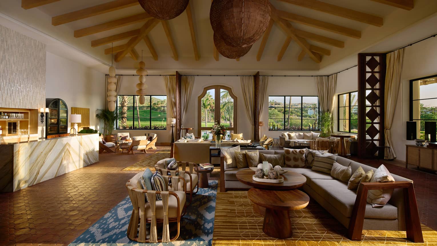 An interior event space with vaulted ceiling, large pendant lighting, large windows, and an assortment of tables and upholstered couches and chairs