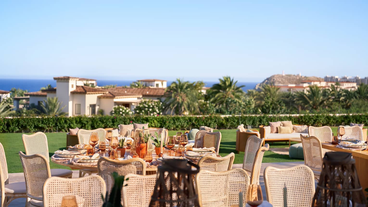 Tables placed and set for an event on a vast lawn, with trees, buildings and the coastal horizon in the background