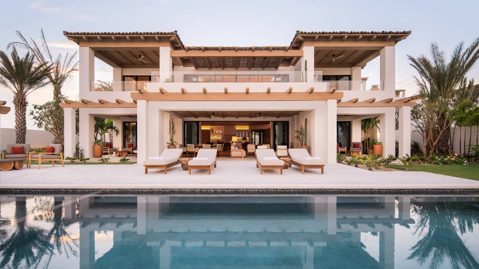 Spanish-style, two-storey villa lined by palm trees and sert behind a pool and deck