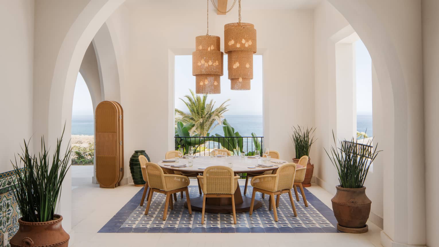 Large, round dining table set beneath a white archway with openings that reveal views of the ocean