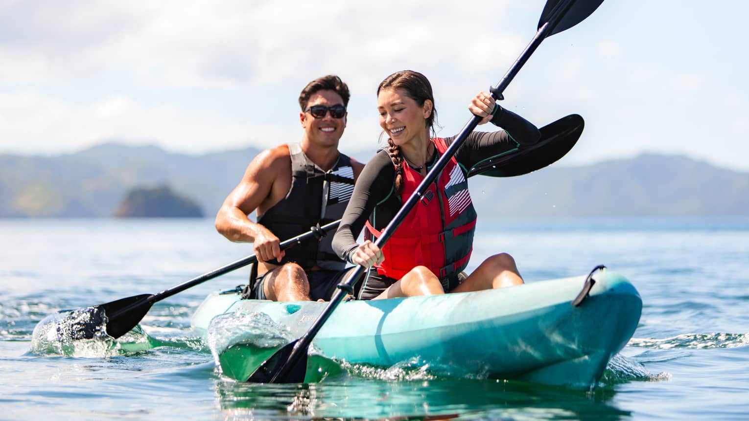 Man and woman smiling and riding in a bright blue kayak in the ocean