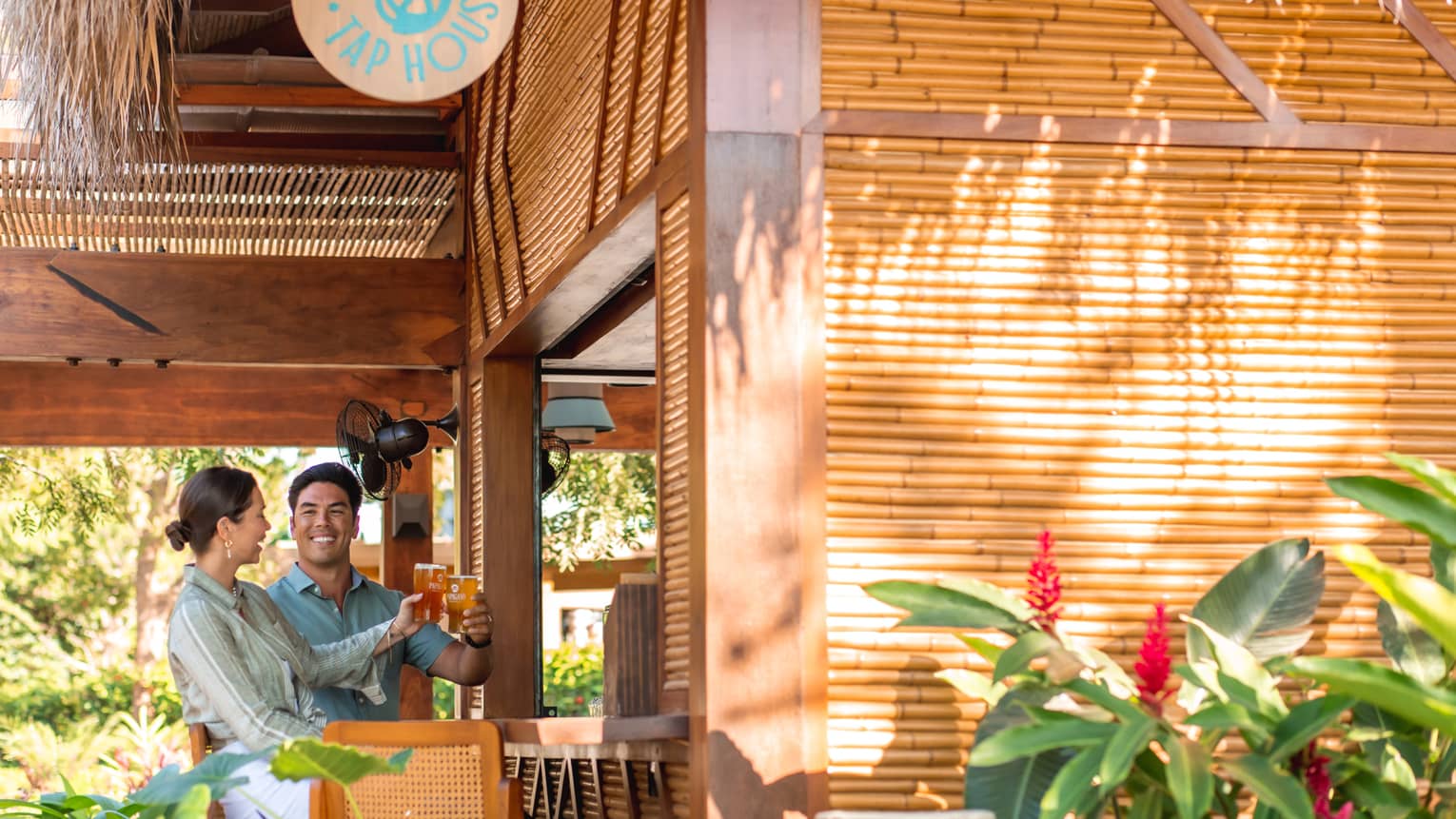 Two people raising a pint of beer to each other at the all-bamboo bar at Palapita Taphouse