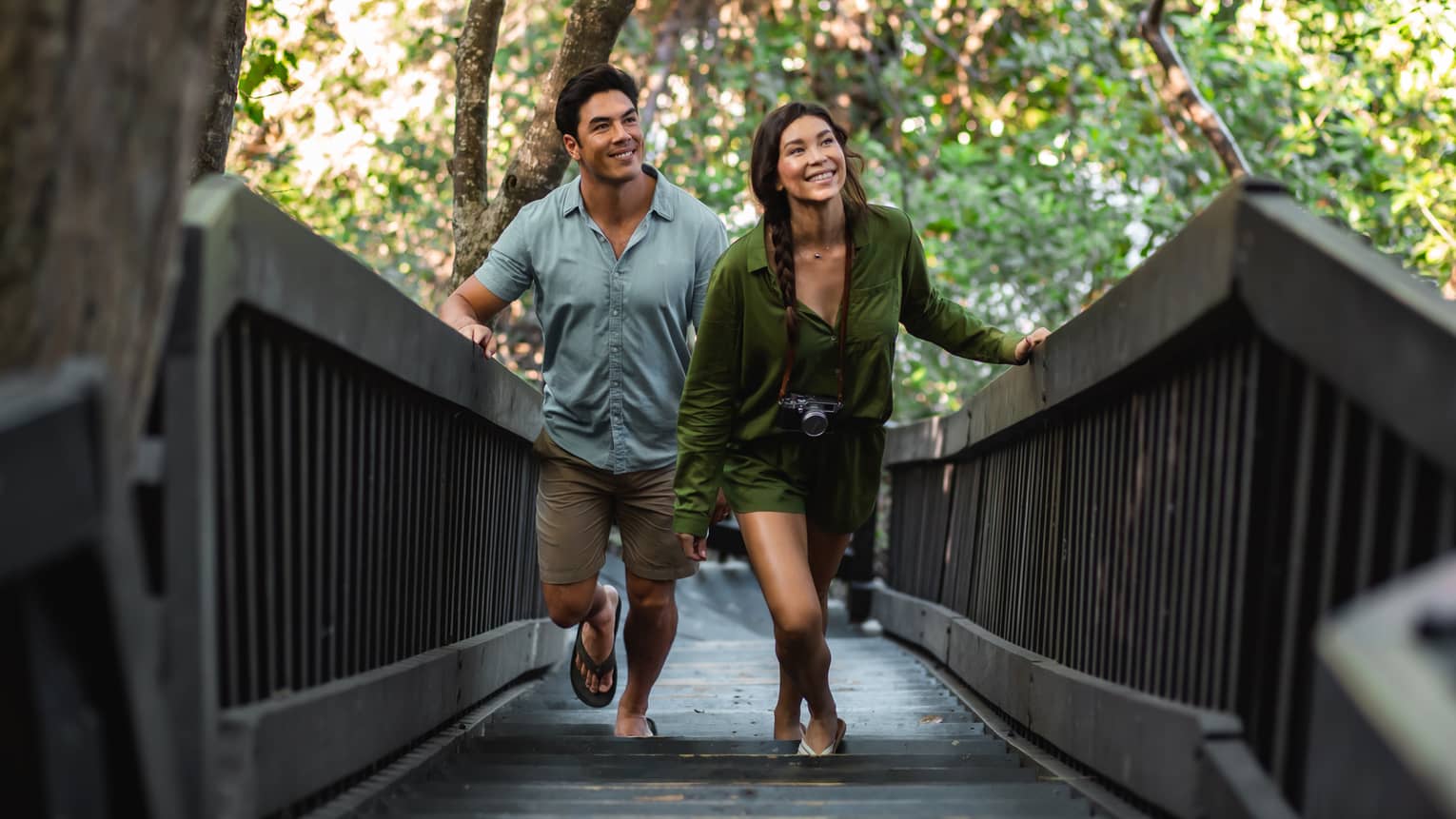 A man and a woman walk up a wooden walkway surrounded by trees