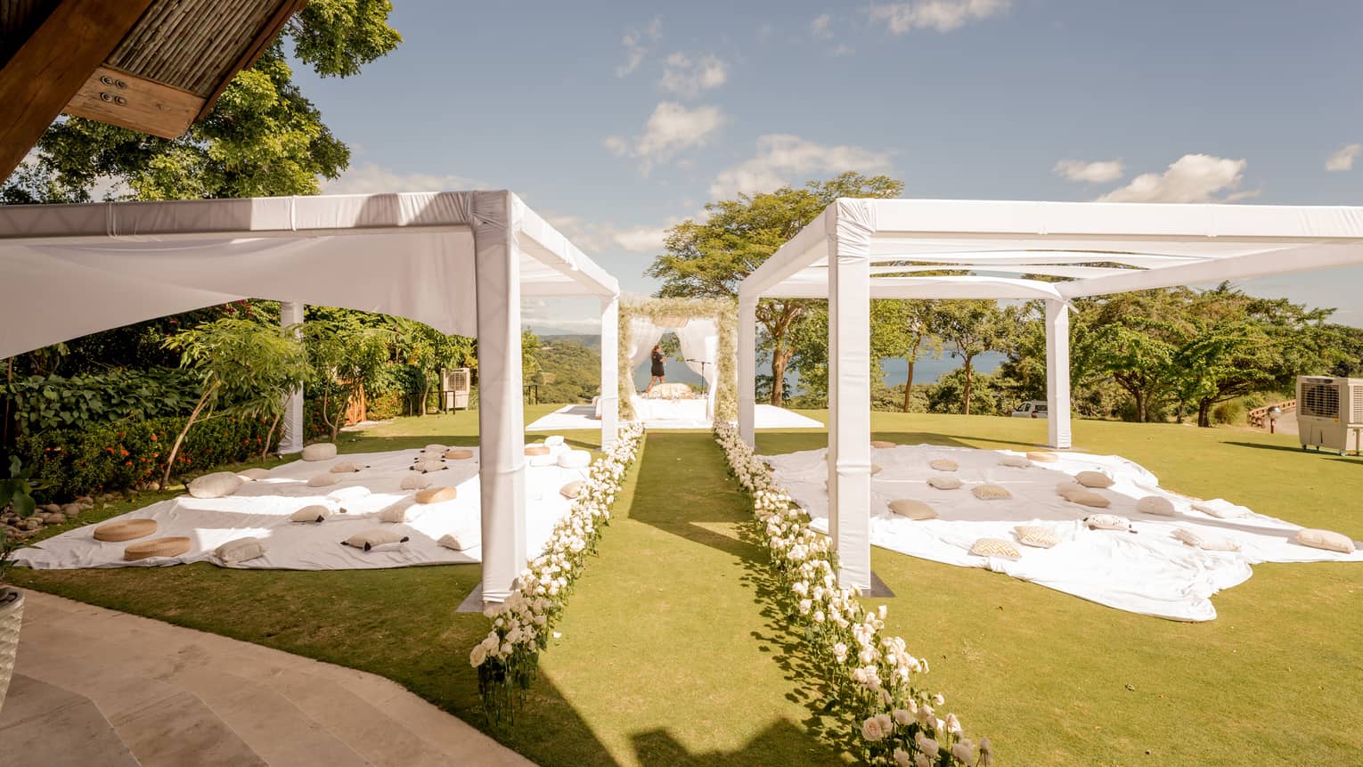 Covered wedding reception area on green lawn, aisle decorated with flowers