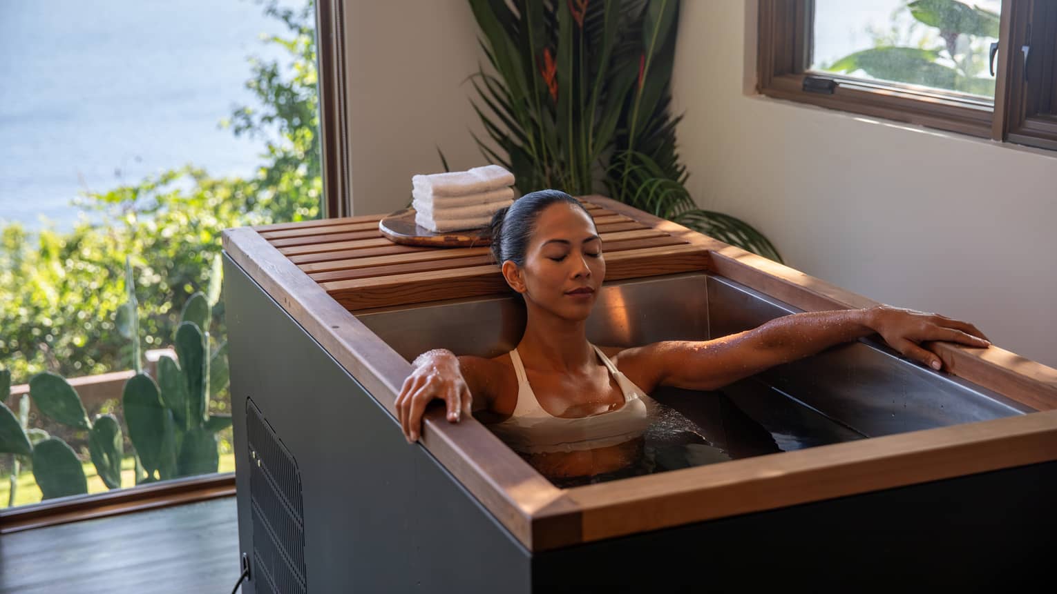 Person sits in a deep soaking tub with a view of the ocean in the background