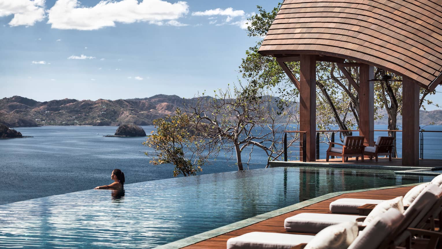 Casa del Cileo Residence Estate patio and wood cabana, woman at edge of infinity pool looking out at ocean