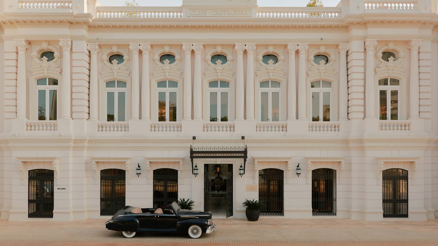 Exterior of a white stone Colonial-style hotel building with a vintage car out front