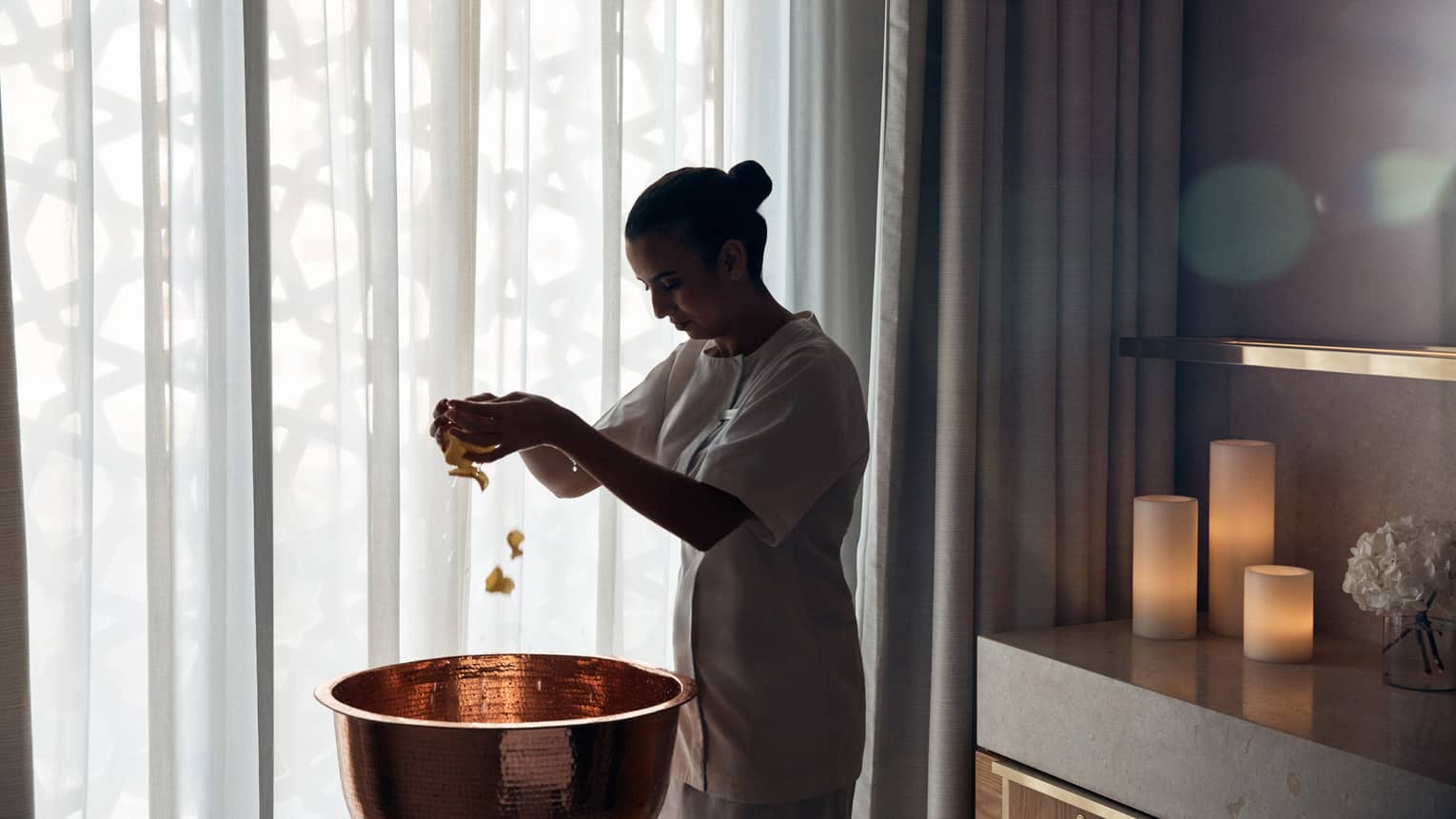 Spa therapist scatters flower petals into a copper basin