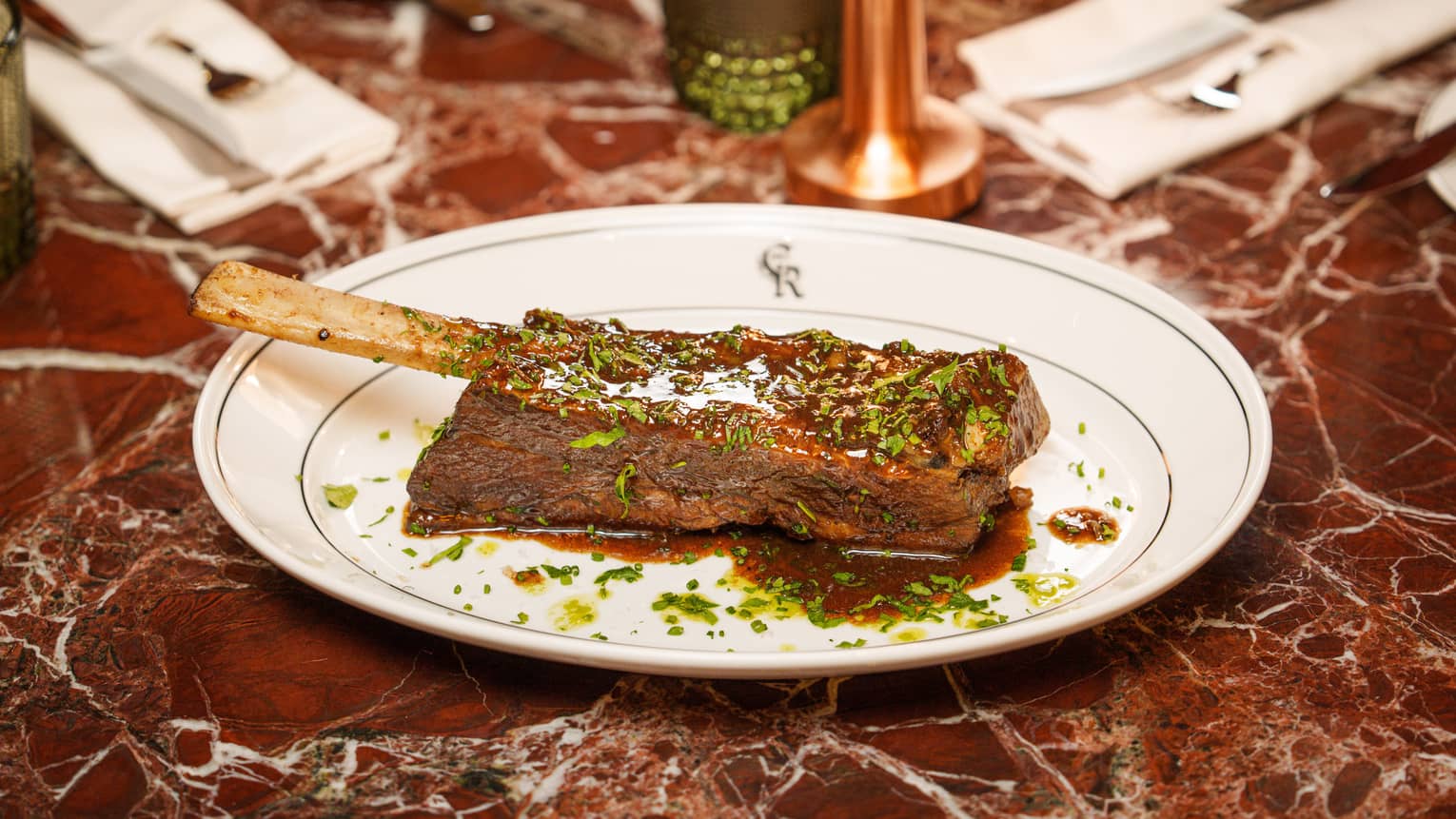 Single Black Angus Braised Short Rib slathered with steak sauce and served on a white plate on top of a burgundy marble table