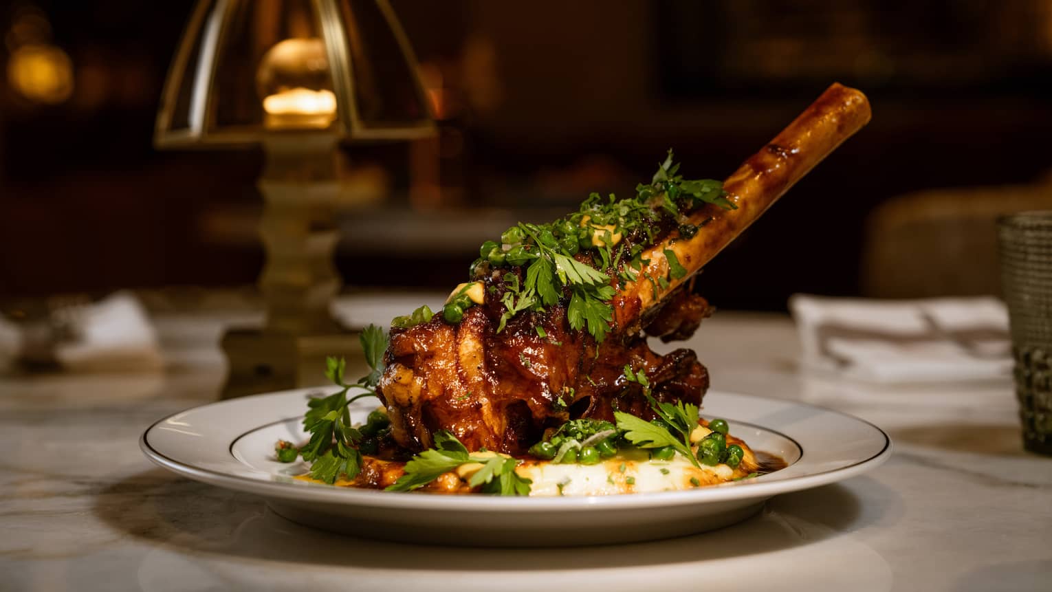 Braised Lamb Shank garnished with fresh parsley and served on a white round dish
