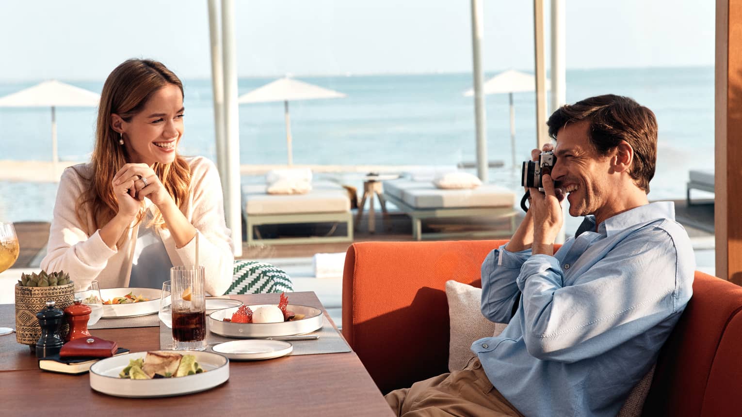 Person holding a camera takes a picture of a person sitting across from them at a restaurant table