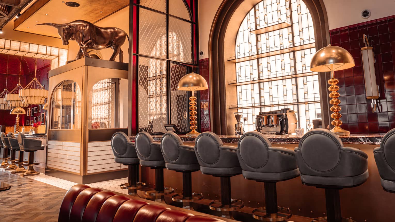 Bar area of a restaurant featuring blue leather bar stools, large brass lighting and 1920s-style decor
