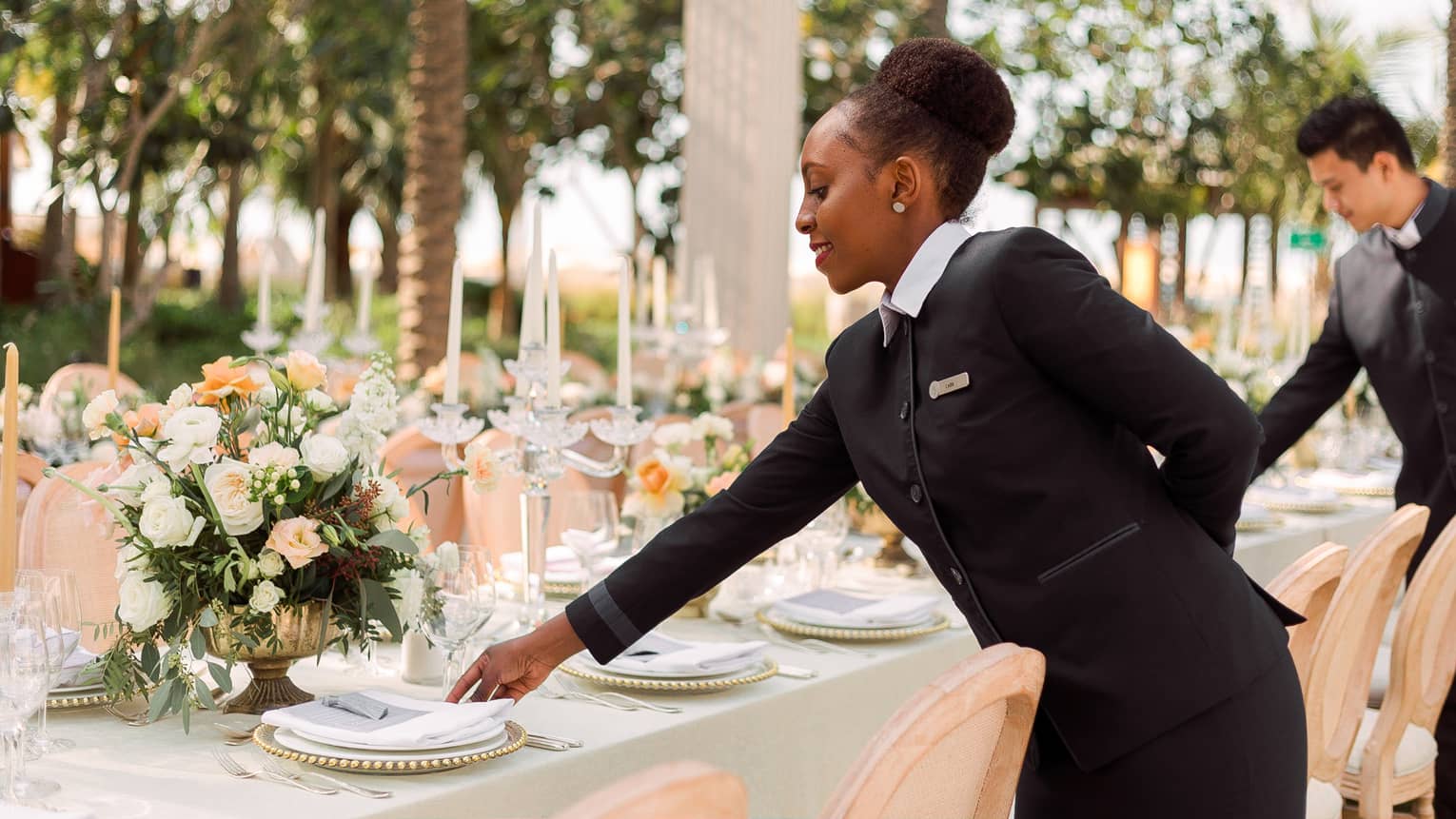 Hotel staff set plates on long banquet table at outdoor wedding reception