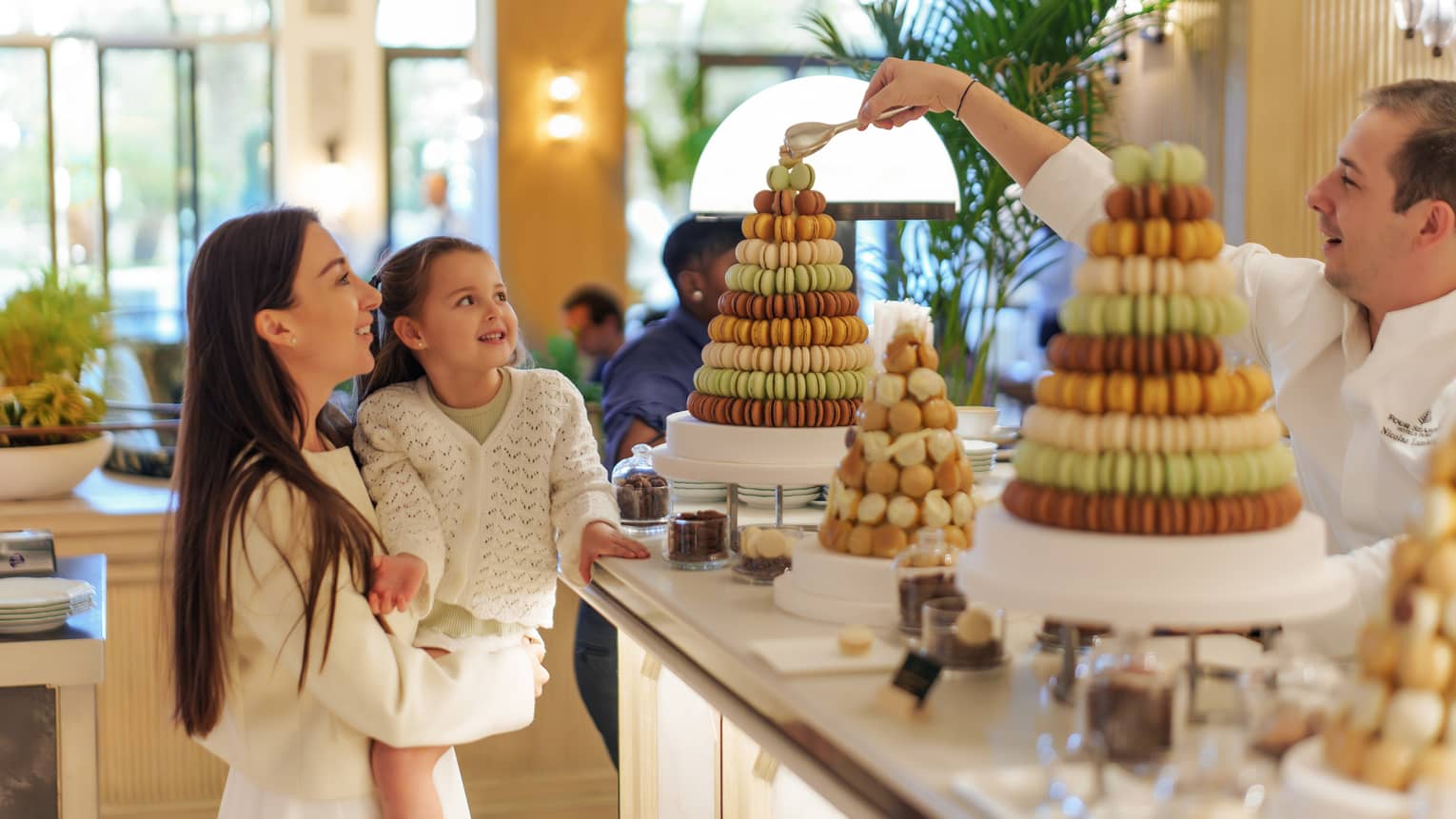 Parent holds a young child in her arms next to a display of macarons