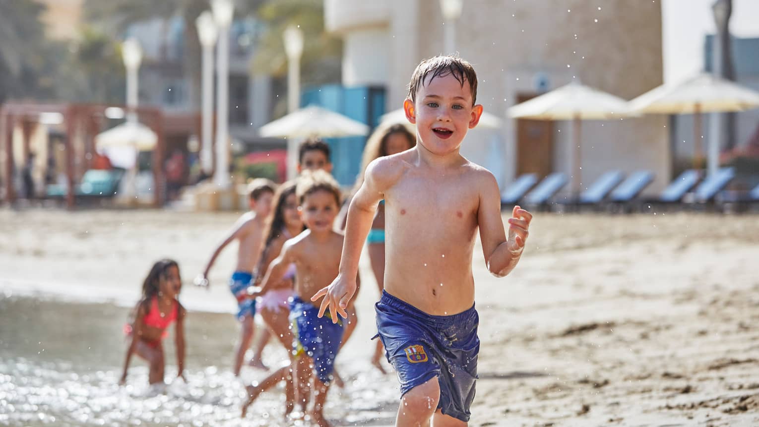 Young children in swimsuits run in a row on sandy beach