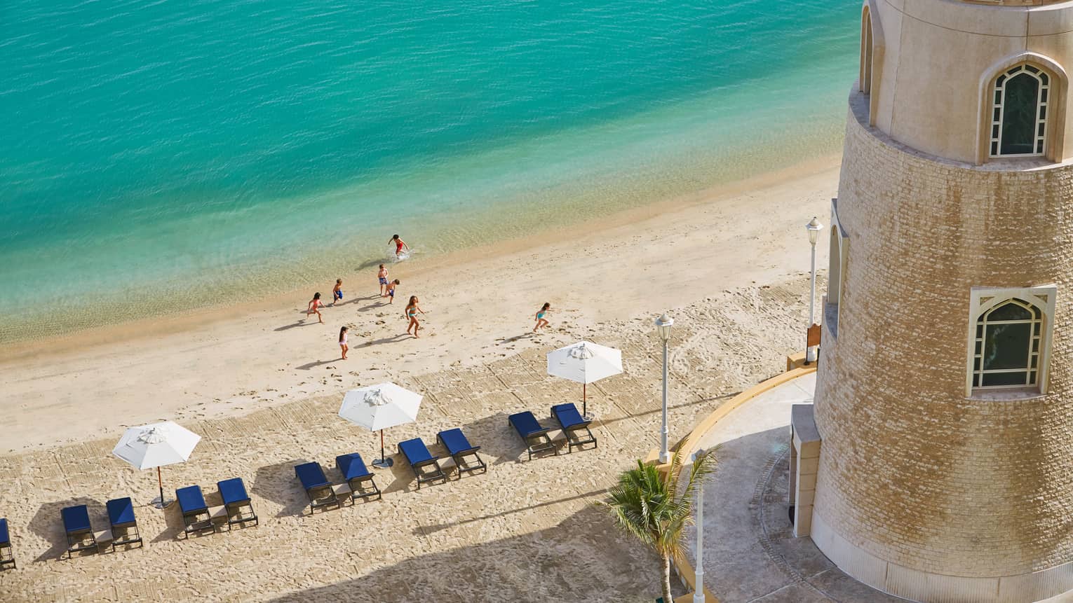 Aerial view of people on beach, row of lounge chairs, beach umbrella