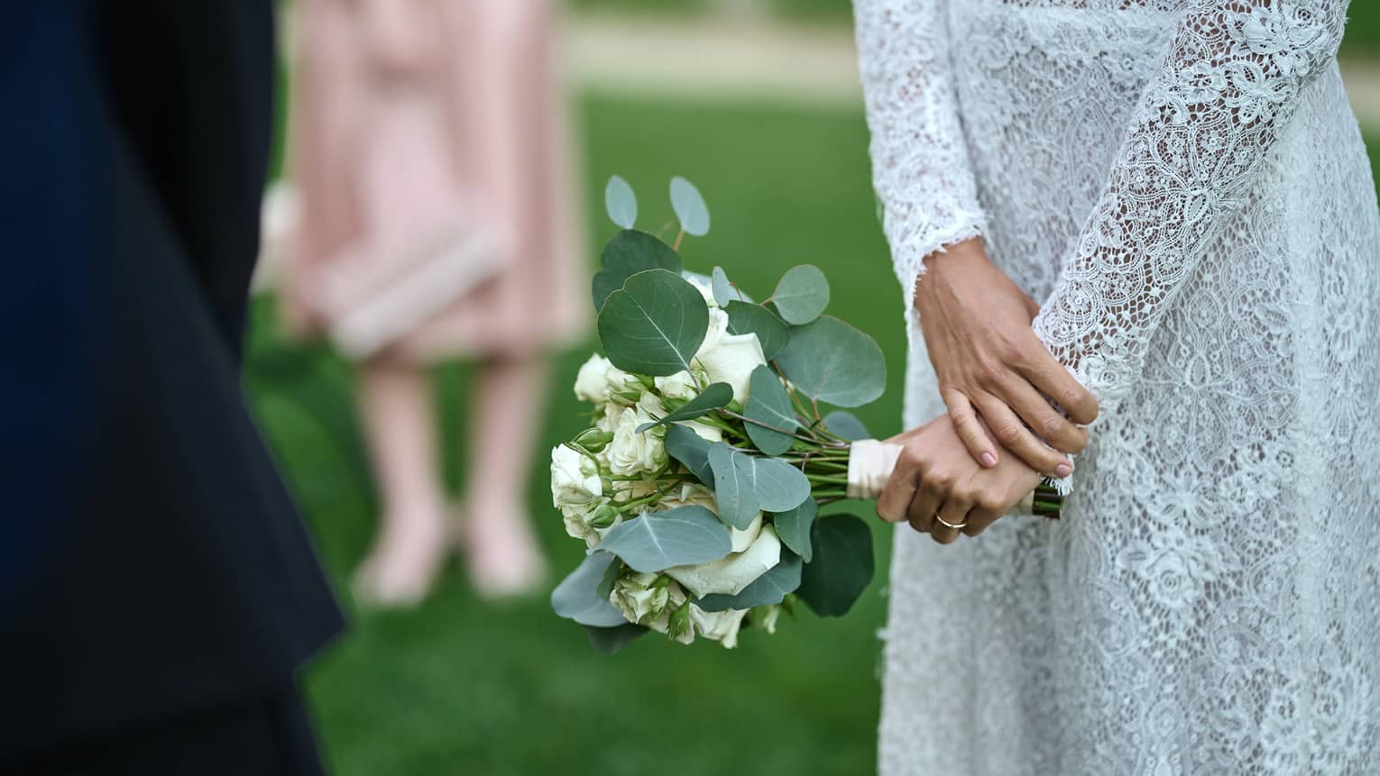 Torso of woman in simple lace wedding gown with hands together holding eucalyptus and white rose bouquet
