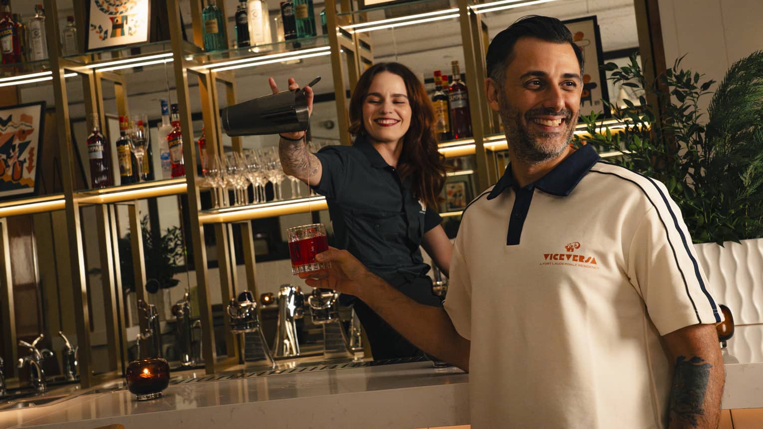 Smiling bartender pours a drink into a glass being held by another smiling person