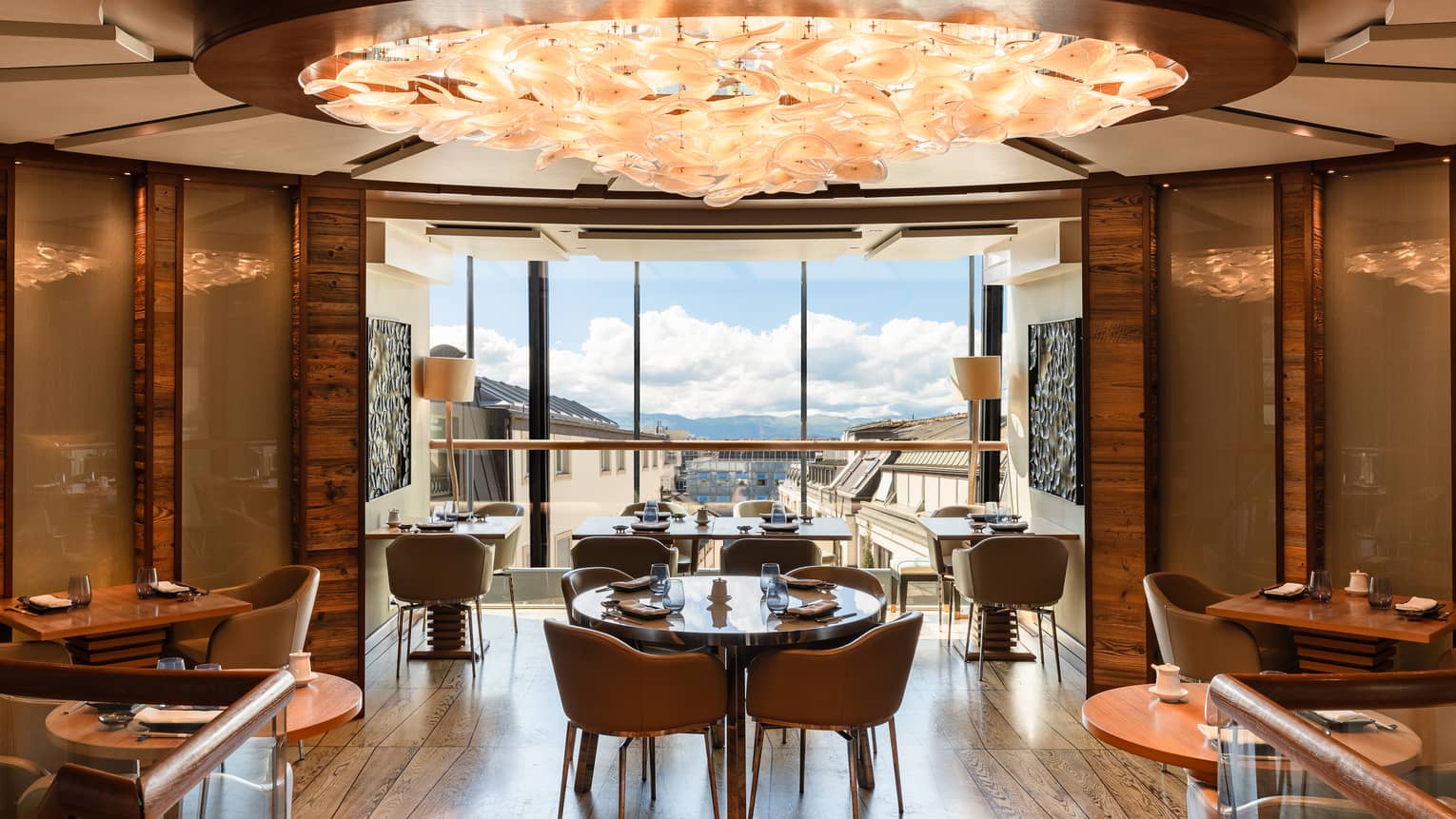 Curved, wood-panelled walls encircle a dining room with a peach-coloured chandelier and windows showing distant mountains.