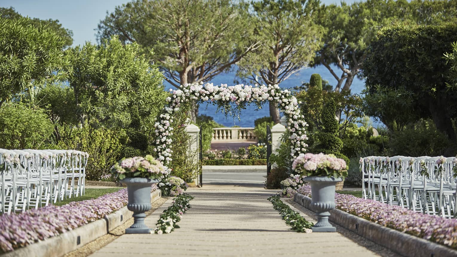 View down sunny garden wedding aisle to flower covered altar