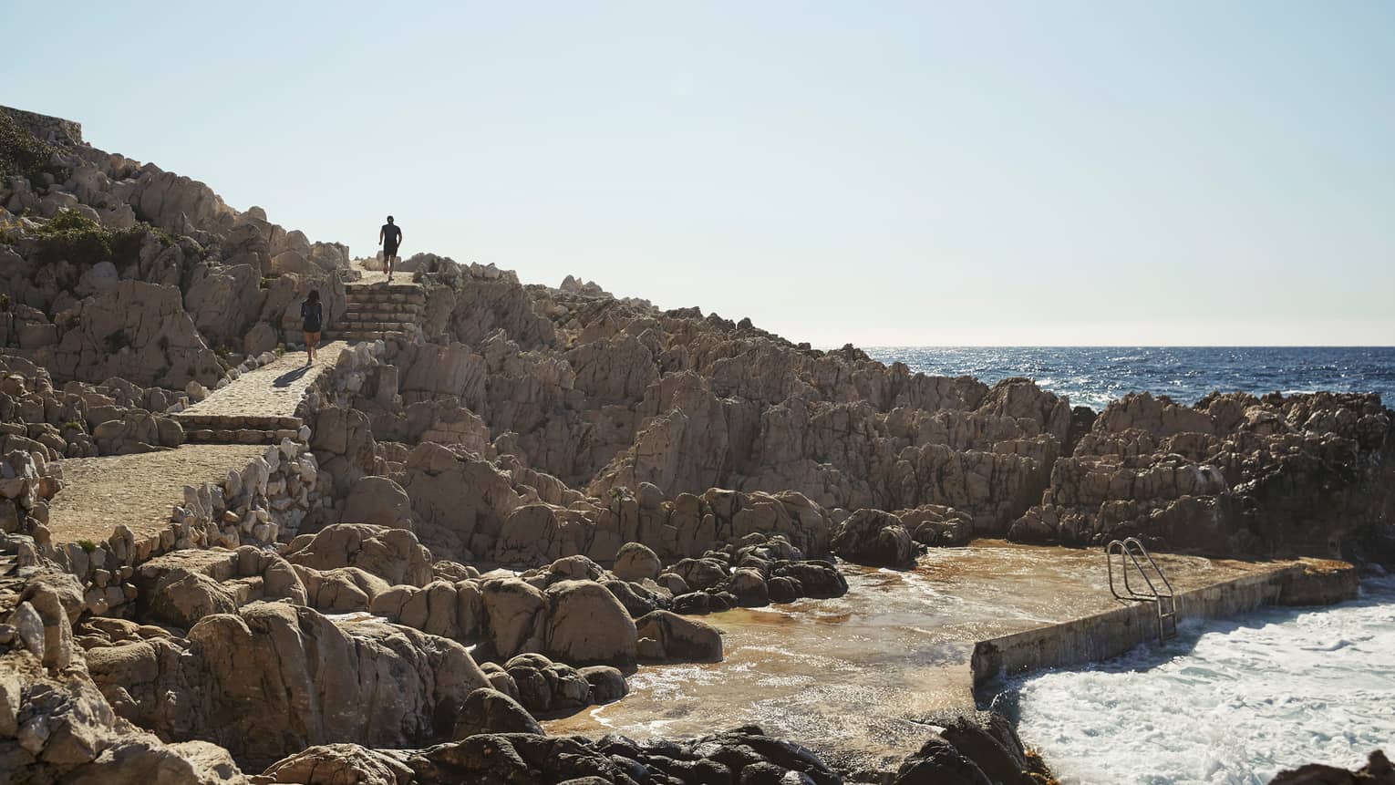 People jog down stone steps to coastal pathways, large rocks, sea
