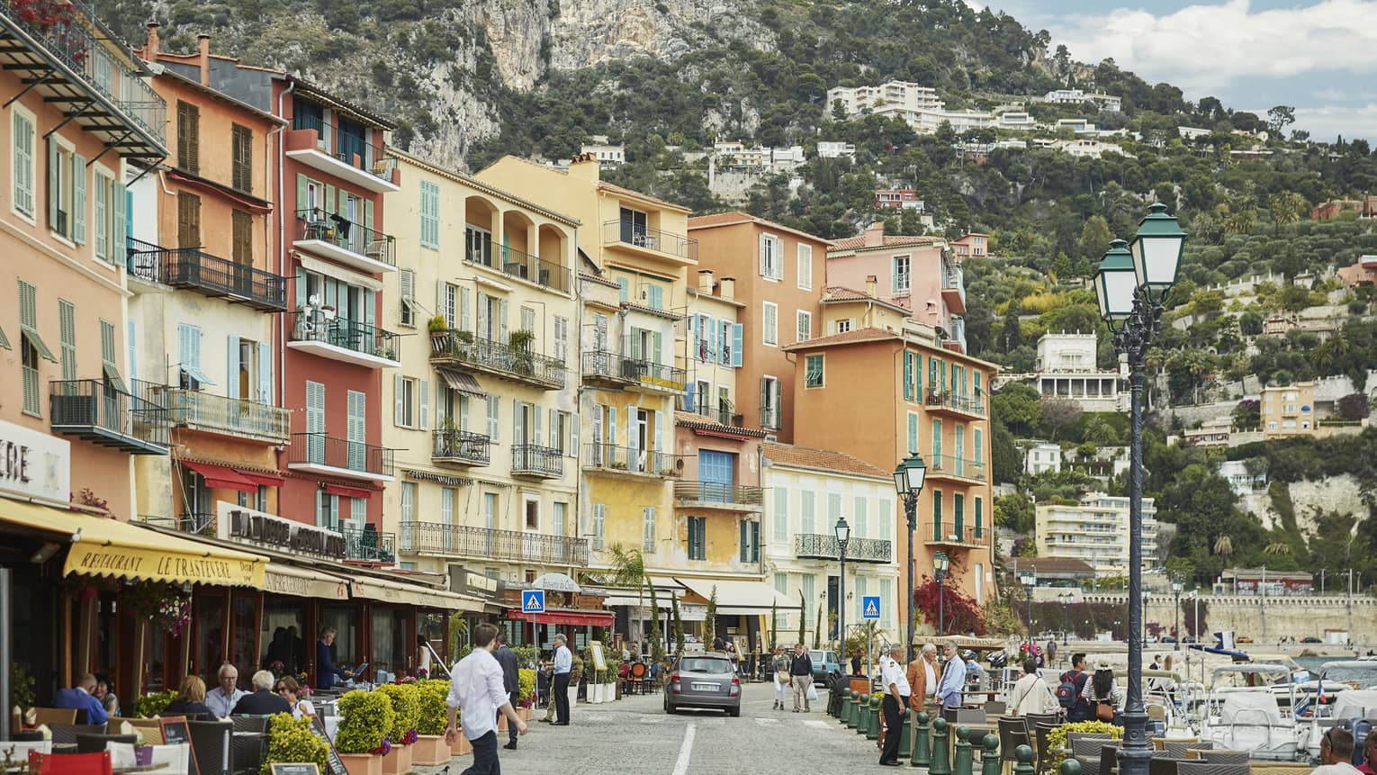 Pedestrians stroll along street, walkways under colourful row buildings, balconies
