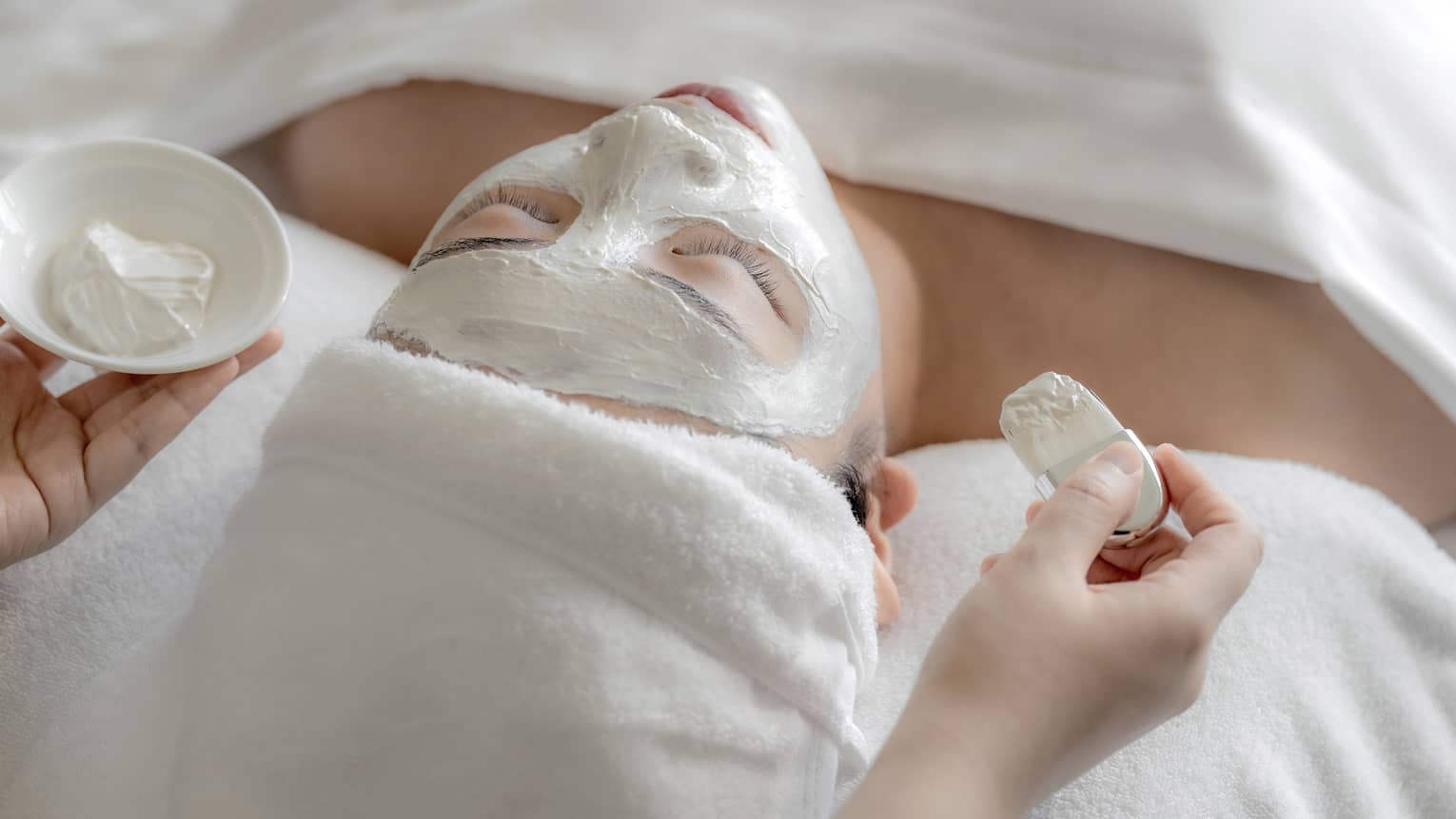Spa therapist applies white clay mask to woman?s face at the Spa
